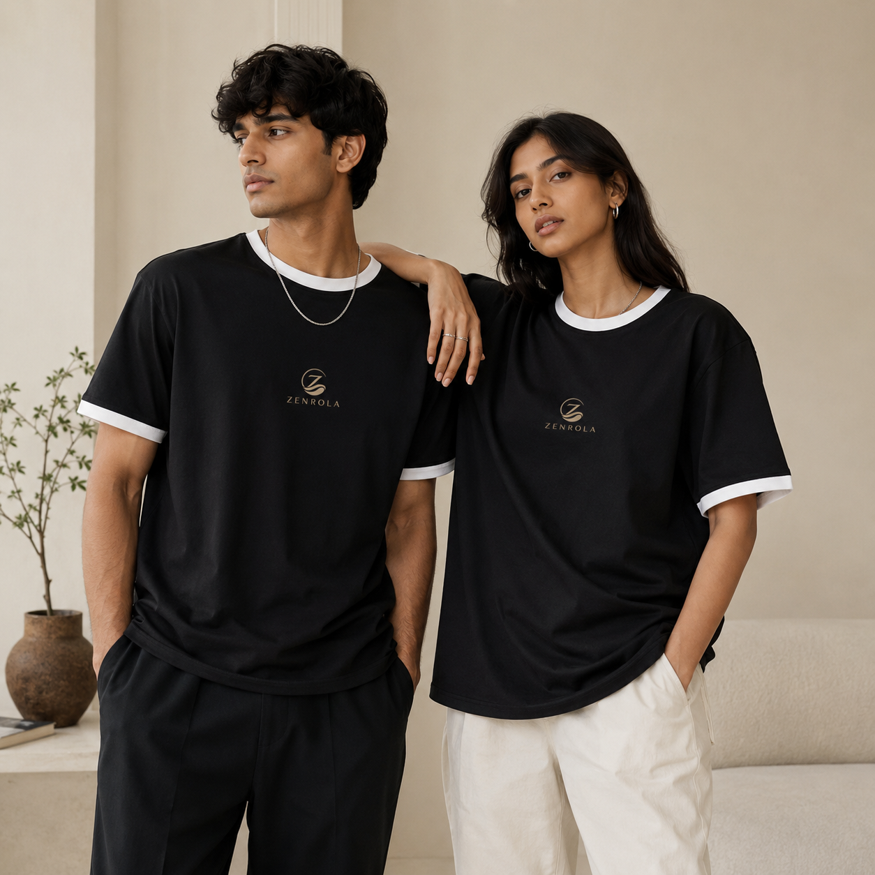 Young Indian man and woman wearing the Zenrola black unisex ringer T-shirt with white ribbed collar and sleeve cuffs in a minimalist beige studio, showcasing a relaxed everyday fit.